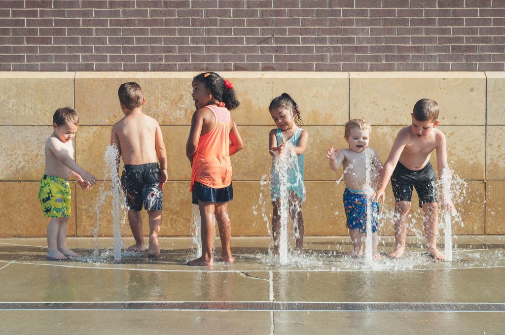 Children of different ages, races, and genders playing a fountain. They are having fun.