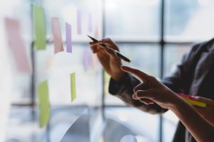 Two people brainstorming together. They are in front post notes on a wall. One is pointing and the other is holding a pen.